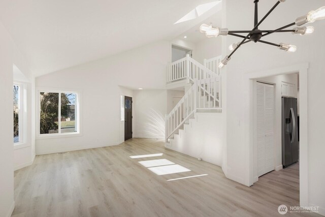 unfurnished living room featuring a chandelier, high vaulted ceiling, stairway, and wood finished floors