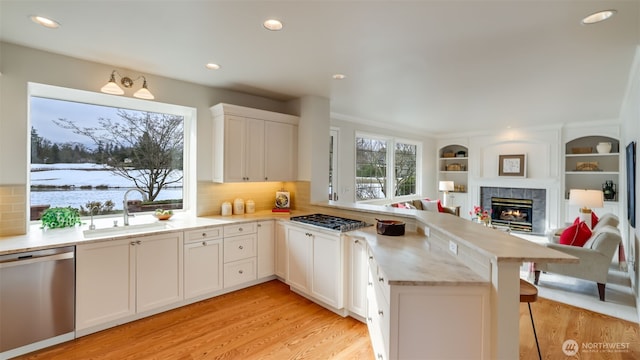 kitchen with stainless steel appliances, a peninsula, a sink, white cabinetry, and light countertops