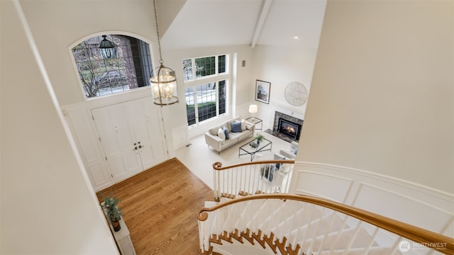 entryway featuring a wainscoted wall, a decorative wall, light wood-style flooring, an inviting chandelier, and a glass covered fireplace