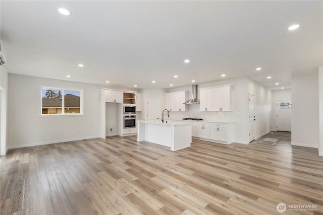 kitchen with light wood-type flooring, appliances with stainless steel finishes, white cabinetry, wall chimney exhaust hood, and a sink