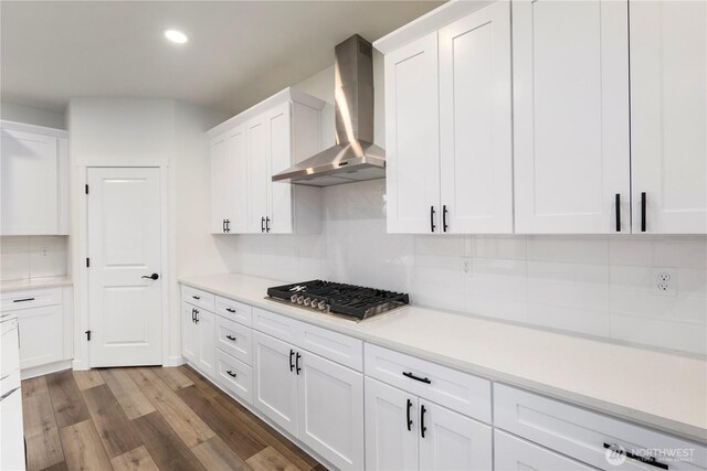 kitchen featuring stainless steel gas stovetop, wood finished floors, white cabinets, and wall chimney range hood