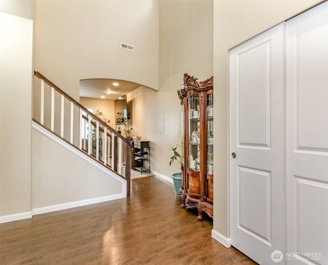 entrance foyer featuring baseboards, visible vents, arched walkways, dark wood finished floors, and stairs