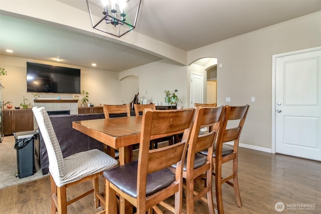 dining area featuring baseboards, a fireplace, arched walkways, and wood finished floors