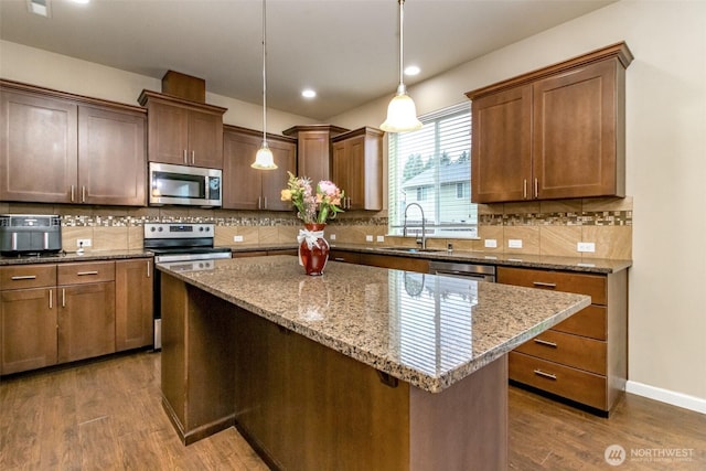 kitchen featuring stainless steel appliances, dark wood-type flooring, a kitchen island, a sink, and hanging light fixtures