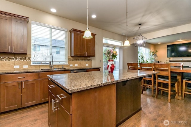 kitchen with pendant lighting, backsplash, a kitchen island, a sink, and wood finished floors