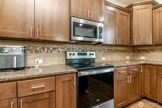 kitchen featuring appliances with stainless steel finishes, brown cabinets, backsplash, and light stone counters