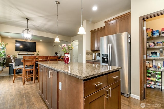 kitchen with arched walkways, a kitchen island, light stone counters, dark wood-style flooring, and stainless steel refrigerator with ice dispenser