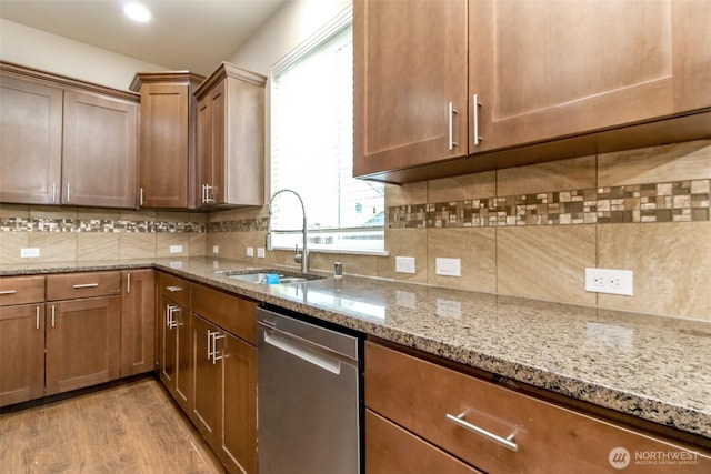 kitchen with decorative backsplash, light wood-style flooring, light stone counters, a sink, and stainless steel dishwasher