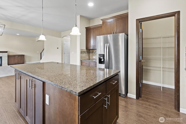 14426 99th Ave SE, Yelm, WA 98597 - kitchen featuring stainless steel fridge with ice dispenser, dark wood-style flooring, arched walkways, a center island, and stone counters