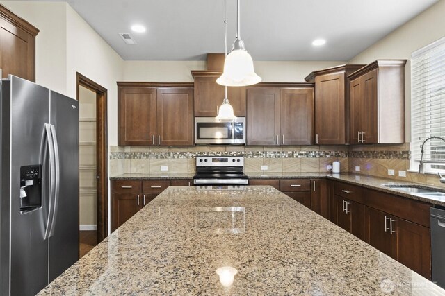 14426 99th Ave SE, Yelm, WA 98597 - kitchen featuring appliances with stainless steel finishes, a sink, hanging light fixtures, decorative backsplash, and light stone countertops