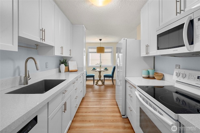 kitchen featuring white appliances, light wood-style flooring, a sink, light countertops, and white cabinets