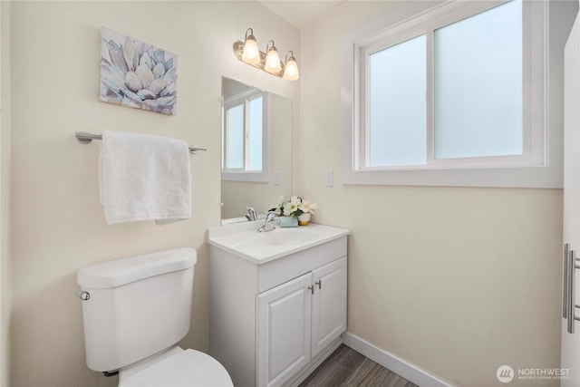 half bath with toilet, vanity, baseboards, and wood finished floors