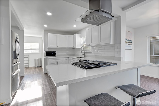 kitchen featuring kitchen peninsula, sink, white cabinets, a kitchen bar, and island range hood