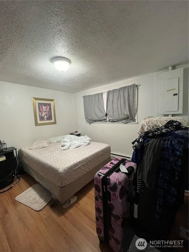 bedroom with hardwood / wood-style flooring, a baseboard radiator, electric panel, and a textured ceiling