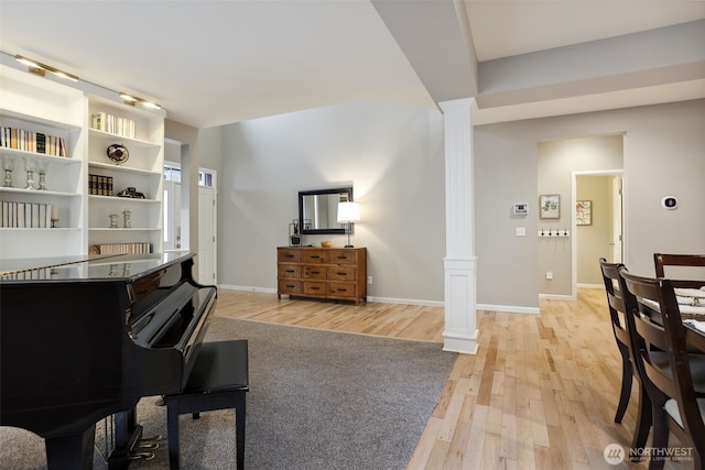 living area with baseboards, light wood finished floors, and ornate columns