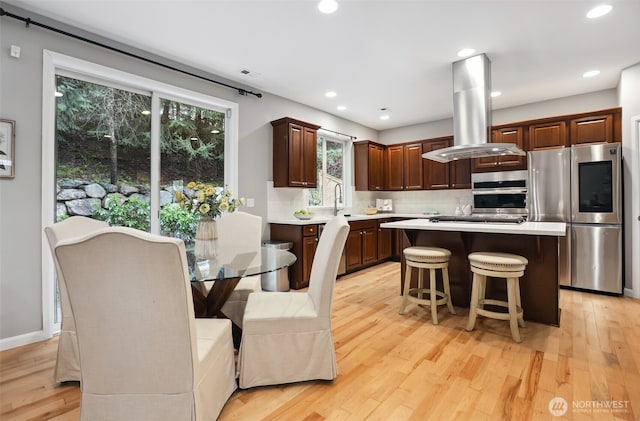 kitchen with stainless steel appliances, tasteful backsplash, light countertops, island range hood, and light wood-type flooring