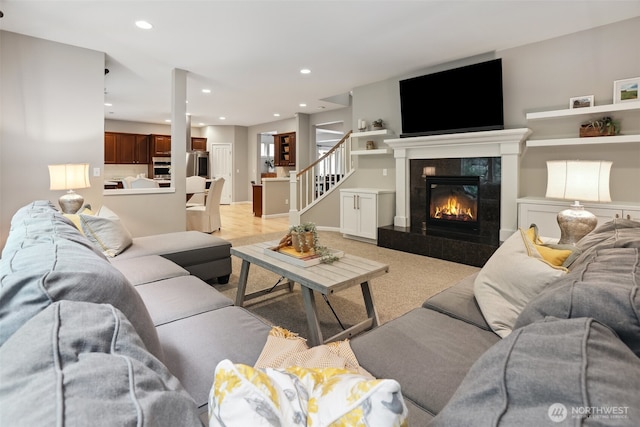 living room with recessed lighting, baseboards, a tiled fireplace, and stairs