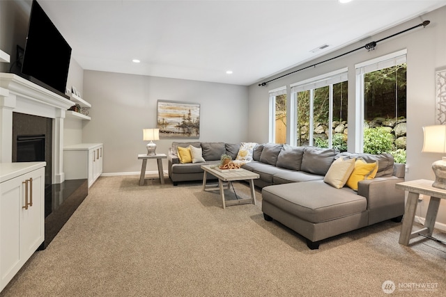 living area with visible vents, baseboards, a glass covered fireplace, light colored carpet, and recessed lighting