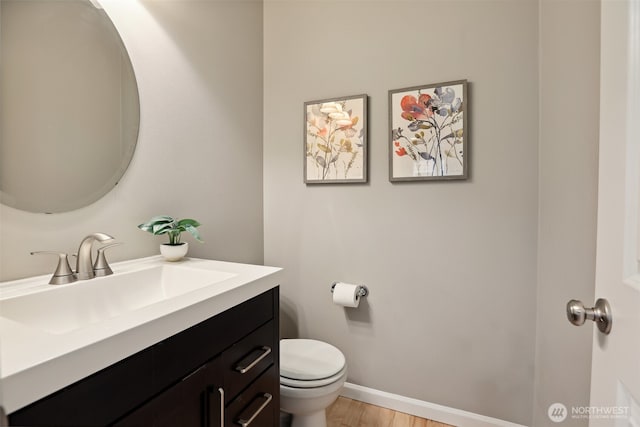 bathroom featuring toilet, baseboards, wood finished floors, and vanity