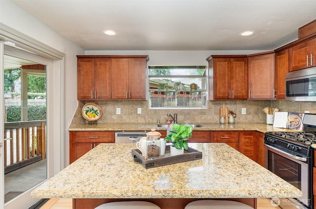 kitchen with light stone countertops, a sink, decorative backsplash, stainless steel appliances, and a center island