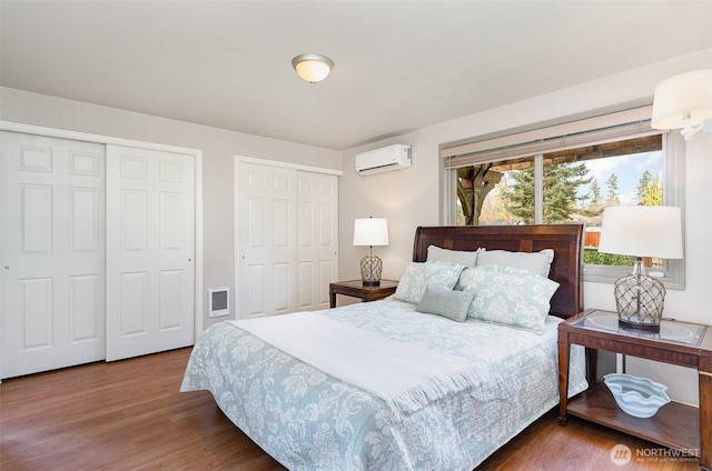 bedroom featuring two closets, a wall mounted AC, and wood finished floors