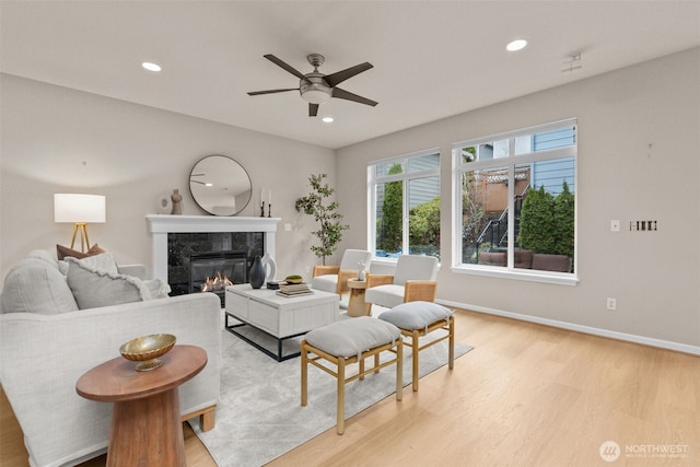 living room featuring a fireplace, light wood finished floors, recessed lighting, ceiling fan, and baseboards