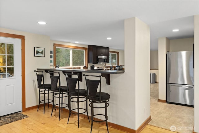 kitchen featuring appliances with stainless steel finishes, a breakfast bar, baseboards, and light wood finished floors