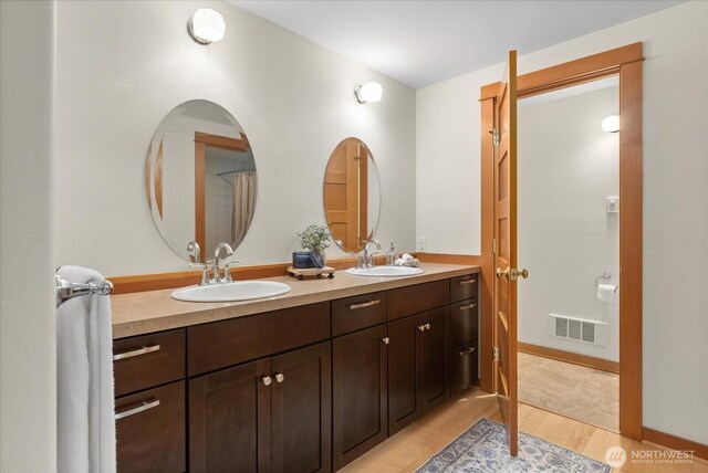 full bathroom with double vanity, wood finished floors, a sink, and visible vents