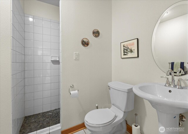 bathroom with baseboards, a tile shower, and toilet