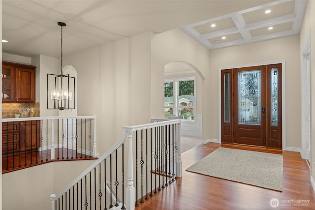 foyer entrance with hardwood / wood-style floors, coffered ceiling, a notable chandelier, and beam ceiling