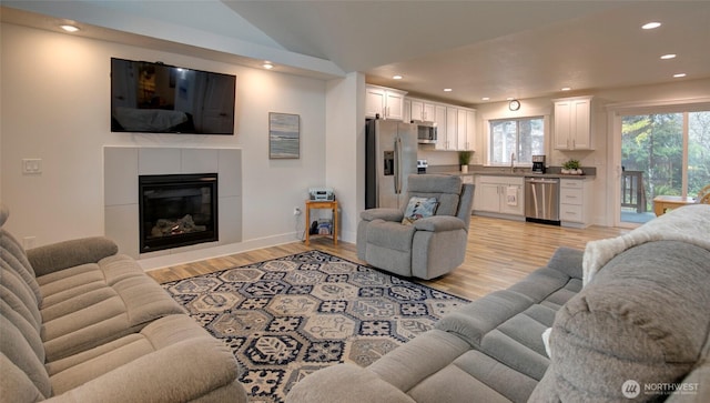 living room with recessed lighting, vaulted ceiling, a fireplace, and light wood finished floors