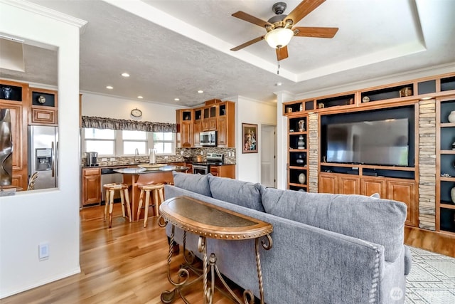 living room featuring a tray ceiling, ceiling fan, sink, and light hardwood / wood-style floors