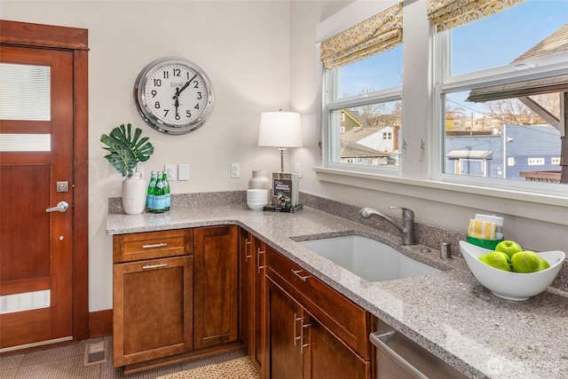 kitchen featuring stainless steel dishwasher, a sink, visible vents, and light stone countertops