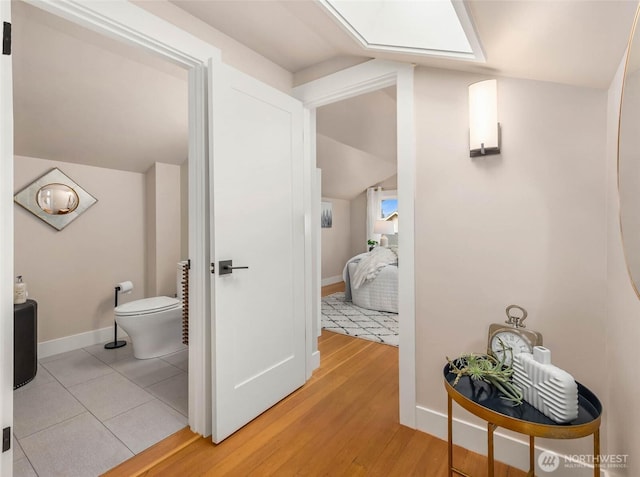 hallway with light wood-type flooring, vaulted ceiling, and baseboards