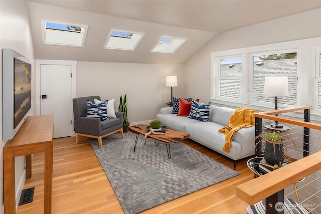 living room featuring vaulted ceiling with skylight, light wood-type flooring, and visible vents