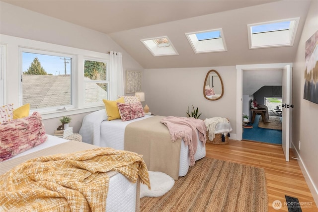 bedroom featuring vaulted ceiling with skylight, light wood-style flooring, and baseboards