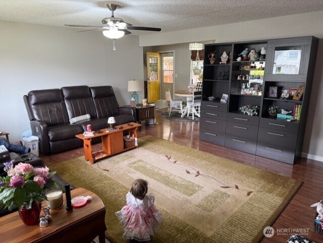 living room with dark hardwood / wood-style flooring, ceiling fan, and a textured ceiling