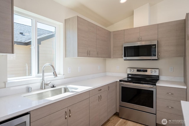 kitchen featuring modern cabinets, appliances with stainless steel finishes, vaulted ceiling, light countertops, and a sink