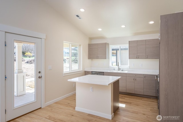 kitchen with a sink, visible vents, vaulted ceiling, light countertops, and a center island