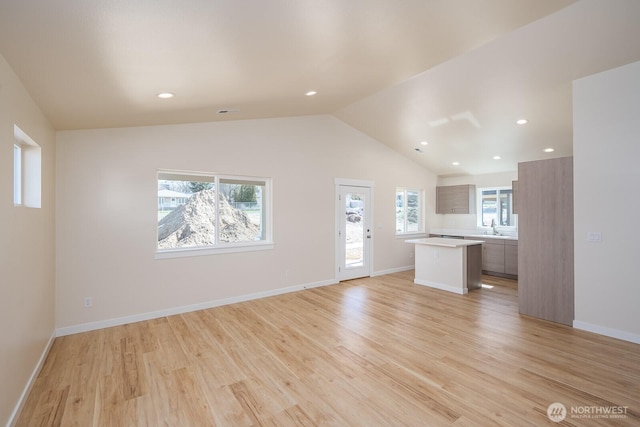 unfurnished living room with baseboards, lofted ceiling, light wood-style floors, a sink, and recessed lighting