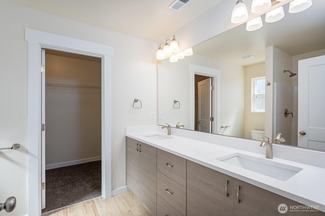 full bath with toilet, visible vents, a walk in closet, and a sink