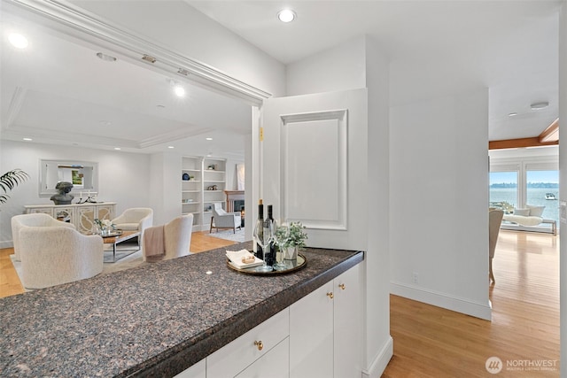 bar with a water view, light hardwood / wood-style floors, a tray ceiling, white cabinetry, and dark stone countertops