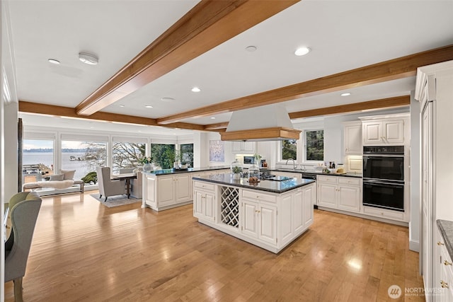 kitchen with premium range hood, black appliances, white cabinets, sink, and a healthy amount of sunlight