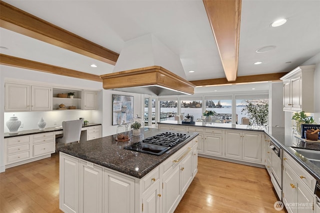 kitchen featuring white cabinetry, black gas stovetop, a kitchen island, custom range hood, and built in desk