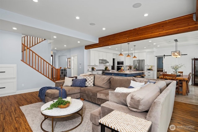 living room with a barn door, beamed ceiling, stairway, and recessed lighting