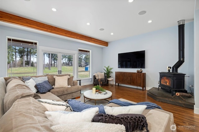 living area featuring beam ceiling, plenty of natural light, wood finished floors, and a wood stove