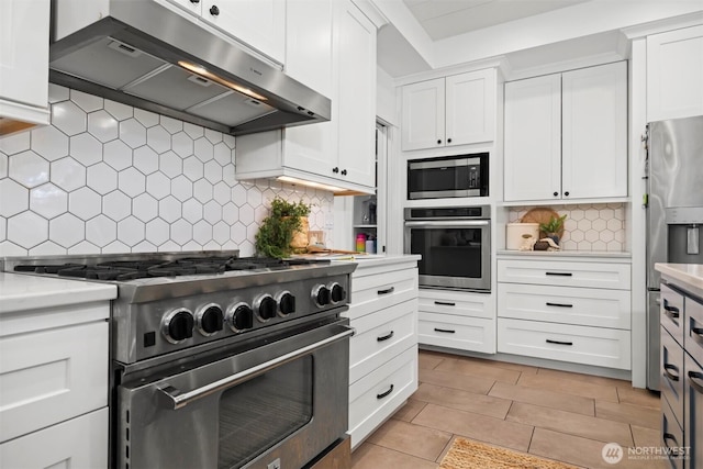 kitchen with light stone counters, range hood, stainless steel appliances, tasteful backsplash, and white cabinetry