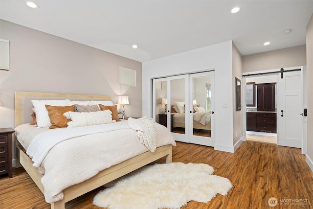 bedroom featuring a barn door, baseboards, wood finished floors, french doors, and recessed lighting