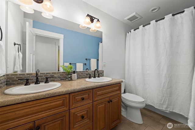 bathroom featuring toilet, tasteful backsplash, double vanity, and a sink