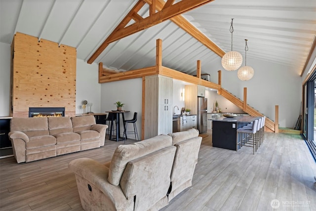 living area with a glass covered fireplace, wood finished floors, an inviting chandelier, high vaulted ceiling, and beam ceiling